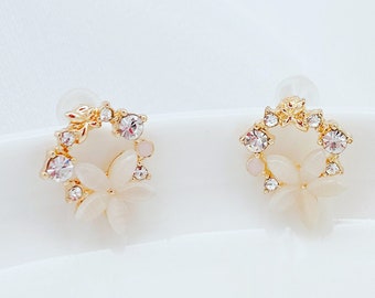 May include: A pair of gold earrings with a delicate floral design. The earrings feature small white flowers with clear rhinestones.