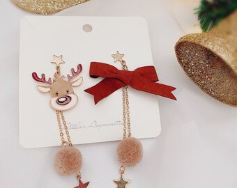 May include: A pair of gold-tone earrings with a reindeer charm and a red velvet bow charm. Each earring has a gold chain with a brown pom-pom at the end. The earrings are displayed on a white card with the text "Juleus Ornaments".