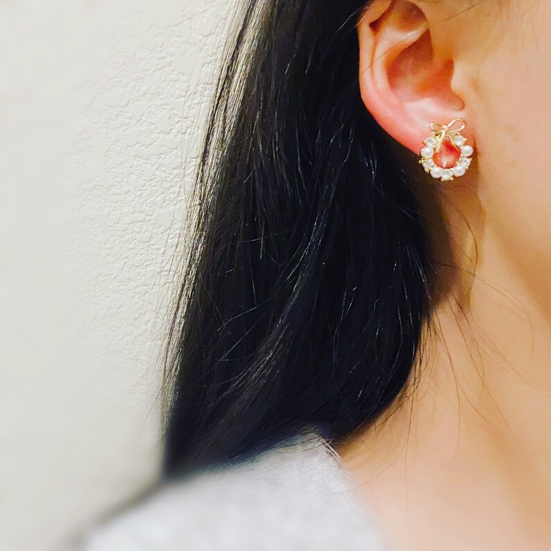 May include: Gold earrings with a pearl and bow design.