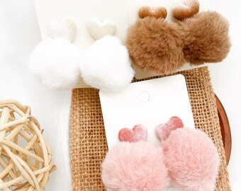 May include: Three pairs of fuzzy heart-shaped hair clips. One pair is white, one pair is brown, and one pair is pink.
