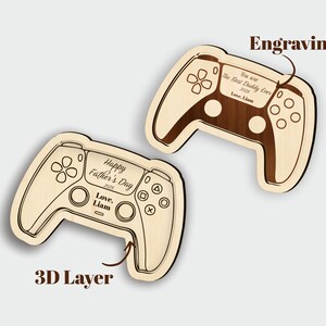 K&ouml;nnte beinhalten: Zwei Holzplatten in Form von Gamecontrollern. Auf einer steht "Happy Father's Day 2025" und "Love, Liam". Auf der anderen steht "You are The Best Daddy Ever 2025 Love, Liam". Beide haben eine 3D-Schicht.