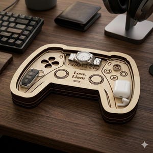 K&ouml;nnte beinhalten: Ein Holztablett in Form eines Gamecontrollers, das eine Uhr, Autoschl&uuml;ssel, Ringe und kabellose Ohrh&ouml;rer enth&auml;lt. Das Tablett ist mit "Father's Day 2025" und "Love, Liam" graviert.