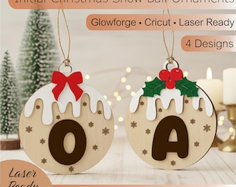 Op de afbeelding: Houten kerstversieringen met de letters "O" en "A". Elke versiering heeft een wit glazuurontwerp, sneeuwvlokken en een rode strik of hulstbessen. De tekst "Initial Christmas Snow Ball Ornaments" staat bovenaan.