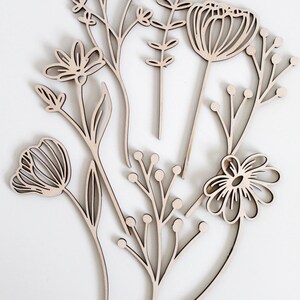 May include: A set of six wooden flower cutouts in a variety of shapes and sizes. The cutouts are all in a natural wood color and have a simple, minimalist design.