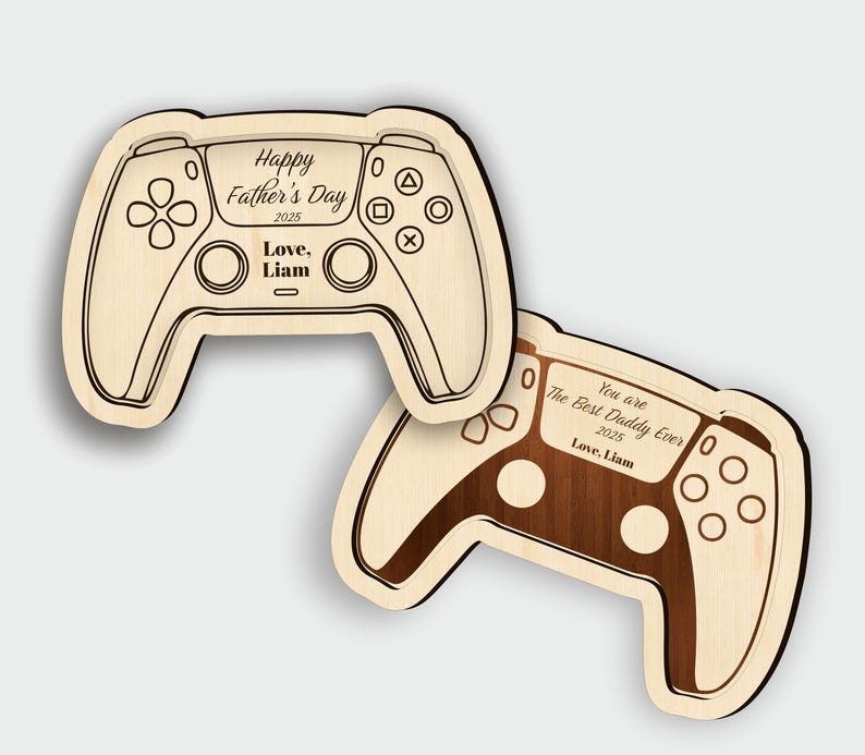 K&ouml;nnte beinhalten: Zwei Holzschilder in Form eines Gamecontrollers. Eines ist hellfarbig mit dem Text "Happy Father's Day 2025 Love, Liam." Das andere ist dunkel gef&auml;rbt mit dem Text "You are The Best Daddy Ever 2025 Love, Liam."