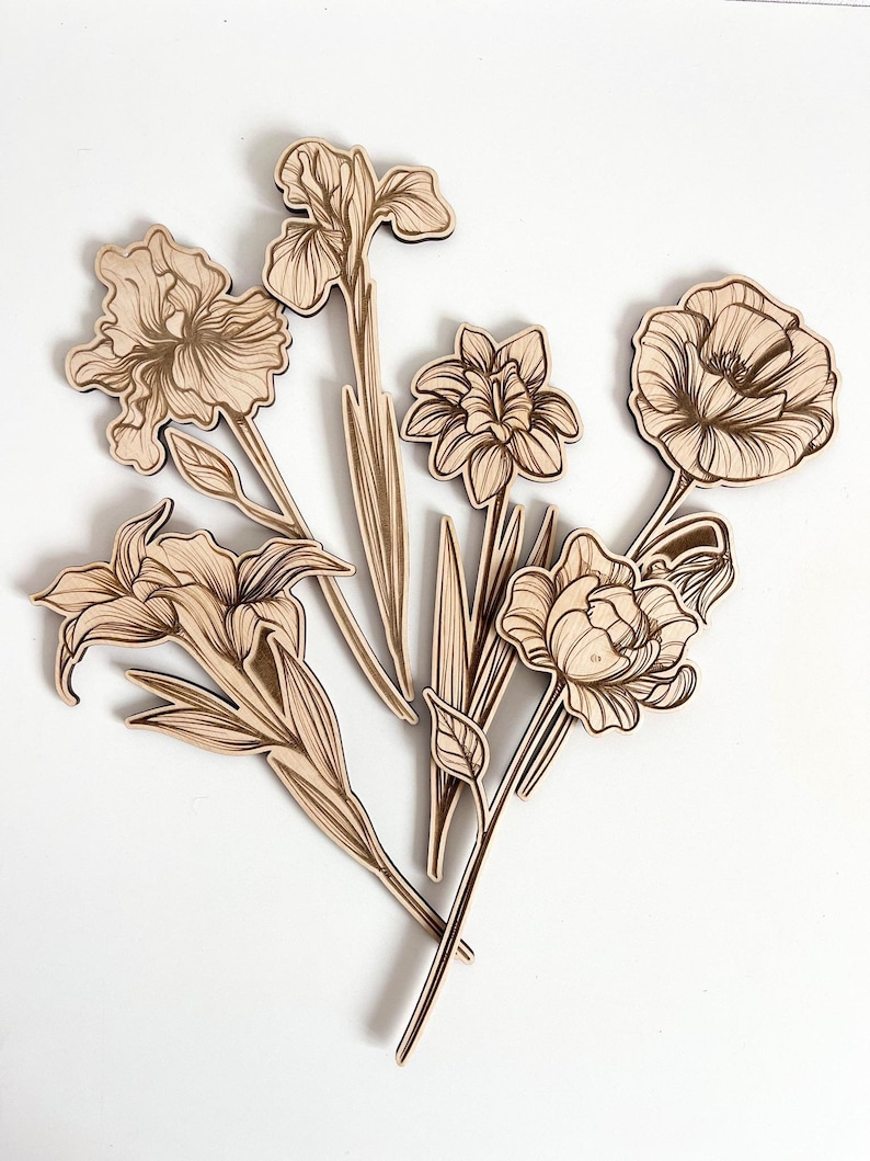 May include: A set of six laser-cut wooden flower shapes, including irises, lilies, and a poppy. The flowers are all in a light brown color and have intricate details.