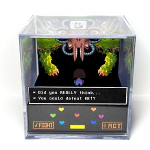 May include: A clear acrylic cube diorama featuring a pixel art scene with a small character facing a large, multi-eyed creature. A black text box displays the words: Did you REALLY think... You could defeat ME!? Below are colorful hearts and buttons.