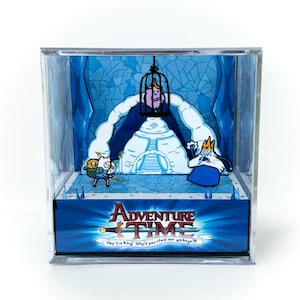 May include: A diorama featuring characters from Adventure Time. The scene includes Finn, the Ice King in a cage, and the Ice King's castle. The Adventure Time logo is displayed on the base, along with the text "Hey Ice King! Why'd you steal our garbage?!"
