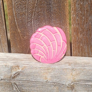 May include: A pink and white concha, a traditional Mexican sweet bread, is shown on a wooden surface.