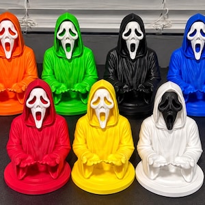 May include: A collection of seven Ghostface character busts, each featuring a white mask and a hooded robe in a different solid color: orange, green, black, blue, red, yellow, and white. Each figure is posed with hands extended forward.