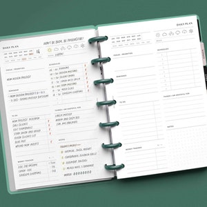 May include: A daily planner with a green cover and a white interior. The planner has a daily plan section, a weekly plan section, and a section for tracking money. The planner also has a section for notes and a section for things to be grateful for. The planner has a motivational quote on the cover that says "Don't be bum, be productive!"