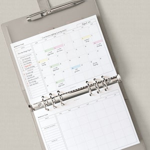 May include: A gray leather bound planner with a silver binder ring system. The planner has a monthly calendar view for August 2023 with handwritten appointments. The planner also has a monthly plan section with a list of goals and tasks.