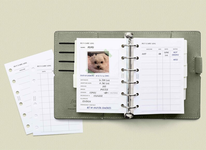 May include: A green leather binder with a white page open to a pet care log. The log includes a photo of a white dog, a section for pet information, and a section for vaccination records.