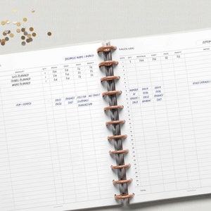 以下が含まれることがあります： 茶色のコイルバインディングが付いた白いプランナー。プランナーには、日付、数量、収益、費用、手数料、利益の列がある売上ログのセクションがあります。プランナーには、事業費と月次利益のセクションもあります。
