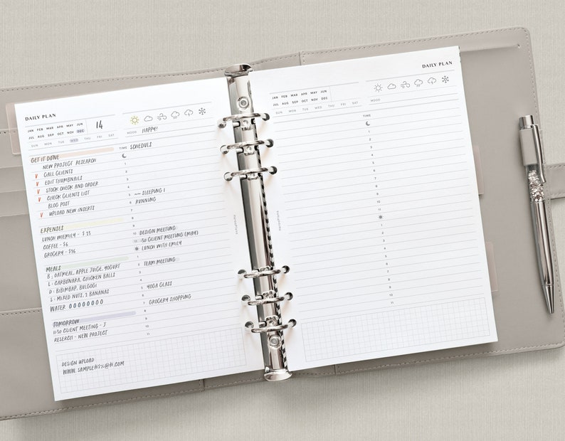 Puede incluir: Una agenda diaria con una cubierta gris y anillos plateados. La agenda est&aacute; abierta en una p&aacute;gina con un plan diario para el 14. La p&aacute;gina tiene una secci&oacute;n para "Get it Done", "Expenses", "Meals", "Water", "Tomorrow" y "Design Affair". La p&aacute;gina tambi&eacute;n tiene una secci&oacute;n para "Time" con una cuadr&iacute;cula para la planificaci&oacute;n.