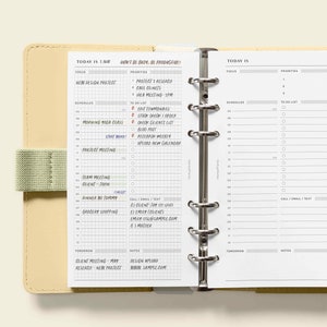 Peut inclure: Un agenda quotidien blanc avec une couverture beige. L'agenda a un reliure &agrave; anneaux et une sangle verte. L'agenda est ouvert &agrave; une page avec la date "Today is 5 Nov" et une liste de t&acirc;ches pour la journ&eacute;e. La page suivante est vierge avec l'en-t&ecirc;te "Today is" et une section pour les priorit&eacute;s, les horaires et une liste de choses &agrave; faire.