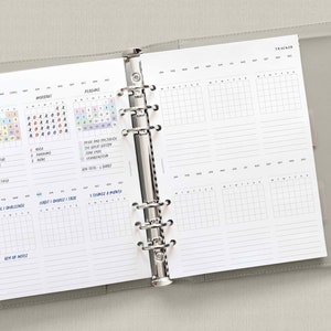 May include: A white planner with a gray cover. The planner has a monthly calendar, a habit tracker, and a goal tracker. The planner is open to a page with a reading tracker and a habit tracker. The planner is a great way to stay organized and on track with your goals.