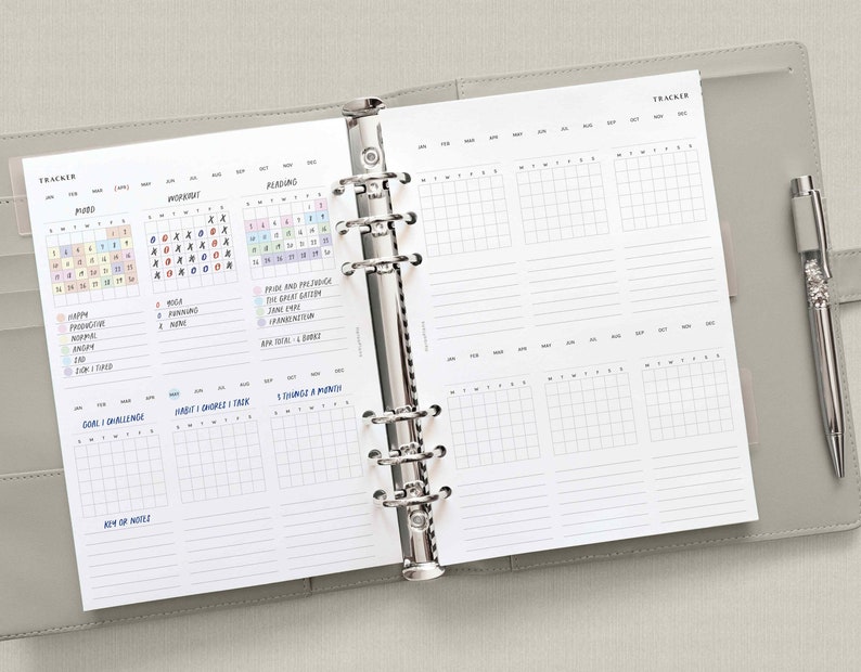 May include: A white planner with a gray cover. The planner has a monthly calendar, a habit tracker, and a goal tracker. The planner is open to a page with a reading tracker and a habit tracker. The planner is a great way to stay organized and on track with your goals.