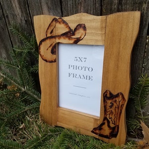 May include: A rustic wooden 5x7 photo frame with a cowboy hat and boot design. The frame is made of natural wood and has a distressed finish. The text "5x7 Photo Frame" is printed on the frame.