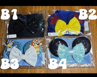 May include: Four different headbands with mouse ears and bows. One black headband with a sequined bow, one blue headband with red and yellow accents, one blue headband with a white bow and cartoon characters, and one black headband with a blue sequined bow.