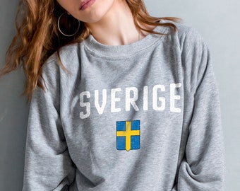 May include: A gray sweatshirt with the word "SVERIGE" printed in white on the front. The Swedish flag is printed below the word.
