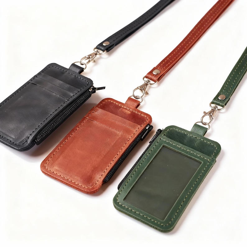 May include: Three leather cardholders with lanyards in black, brown, and green. Each cardholder has a zipper closure and a silver-tone clasp. The green cardholder has a clear window.