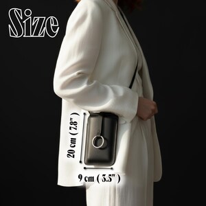 May include: Black crossbody phone bag with a silver ring detail. The bag is 7.8 inches (20 cm) tall and 3.5 inches (9 cm) wide. The word "Size" is written in white script at the top left.