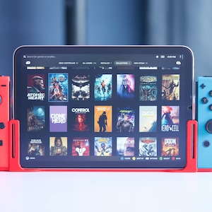 Könnte beinhalten: Ein roter und blauer Gamecontroller mit einem Tablet-Bildschirm, auf dem eine Liste von Videospielen angezeigt wird. Die Spiele umfassen "Atomic Heart", "Clone Hero", "Control", "Dead Space", "Destiny 2", "Doom", "E.T. Phone Home", "Grand Theft Auto V", "Hades", "Red Dead Redemption 2", "The Elder Scrolls V: Skyrim", "The Witcher 3: Wild Hunt" und "Valheim".