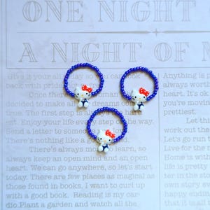 May include: Three blue beaded bracelets with a white Hello Kitty charm on each. The charms have red bows and blue eyes.