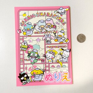 May include: A pink notebook with a colorful illustration of Sanrio characters painting. The characters include Hello Kitty, Pompompurin, Little Twin Stars, and others. The notebook has the text "Sanrio Characters" and "メルヘン" in Japanese.