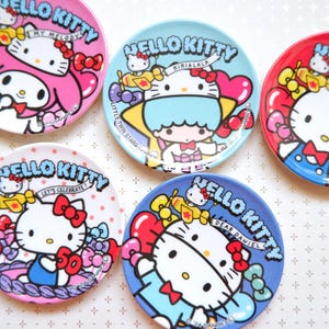 May include: Five Hello Kitty themed ceramic plates with different designs. Each plate features a different Hello Kitty character with a unique background and text. The plates are all white with colorful designs.