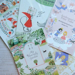 May include: A set of five illustrated cards featuring fairy tales. The cards are decorated with colorful illustrations and text. The text on the cards includes "Grimm's Fairy Tales", "My Heavenly Garden", and "Andersen's Fairy Tales".