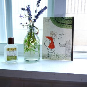 May include: A clear glass bottle with a brown lid filled with lavender flowers and green stems. A small bottle of tea tree oil is next to the vase. A book with the title "Shimai Koibito" is on the windowsill behind the bottles.