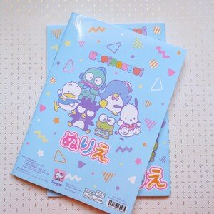 May include: Two blue notebooks with colorful geometric patterns and cartoon characters. The front cover features a group of cartoon characters including a penguin, a frog, a duck, and a monster. The text on the cover reads "Happidanbui" and "みりえ".