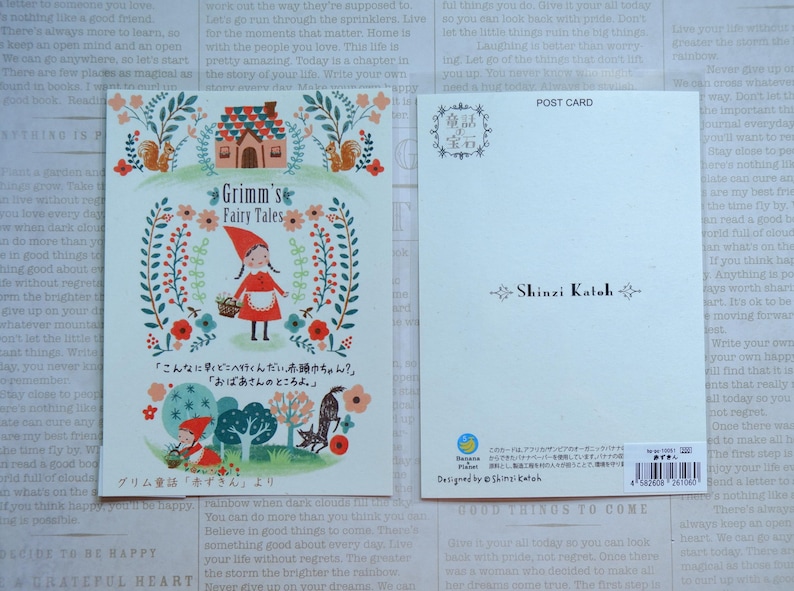 May include: A postcard featuring a colorful illustration of Little Red Riding Hood walking through a forest with a basket of flowers. The text "Grimm's Fairy Tales" is written in a whimsical font. The back of the postcard has a Japanese text and the name "Shinzi Katoh" printed in black.