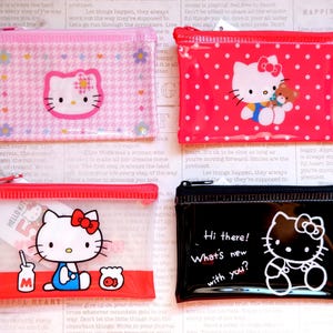 May include: Four rectangular zippered pouches featuring the Hello Kitty character. The pouches are pink, red, and black, with various designs including polka dots, a floral pattern, and text that reads "Hi there! What's new with you?"