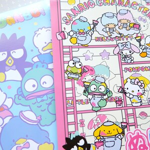 May include: A pink and white notebook with a Sanrio character theme. The cover features Hello Kitty, Pompompurin, and other Sanrio characters painting on a ladder. The text "Sanrio Characters" is printed in black on the cover.