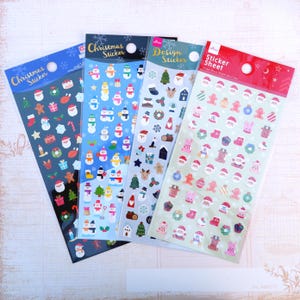 May include: Four sheets of Christmas stickers featuring various holiday designs. The stickers include snowmen, Santa Claus, Christmas trees, wreaths, and other festive elements. The stickers are packaged in clear plastic sleeves with colorful backgrounds.