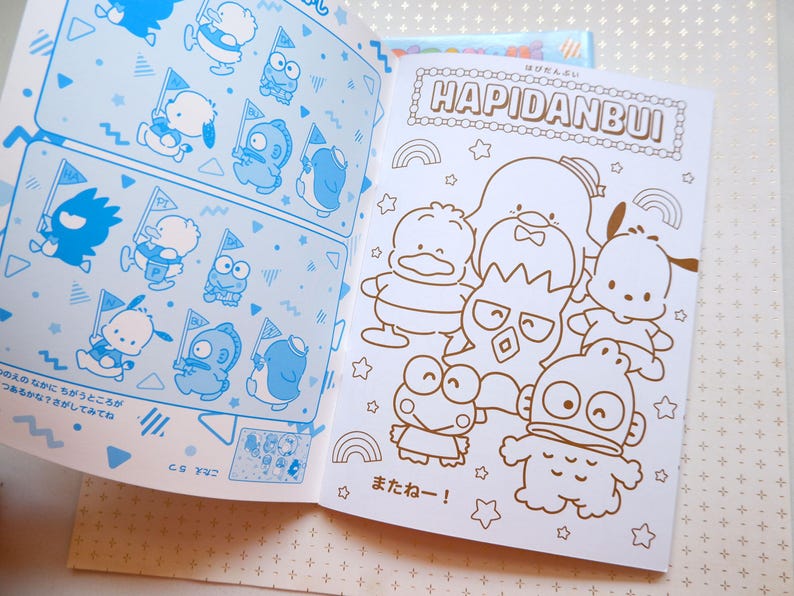May include: A coloring book featuring a group of cartoon characters, including a penguin, a frog, and a bear. The book is titled "Hapidanbui" and has a rainbow design. The characters are outlined in black and ready to be colored in.