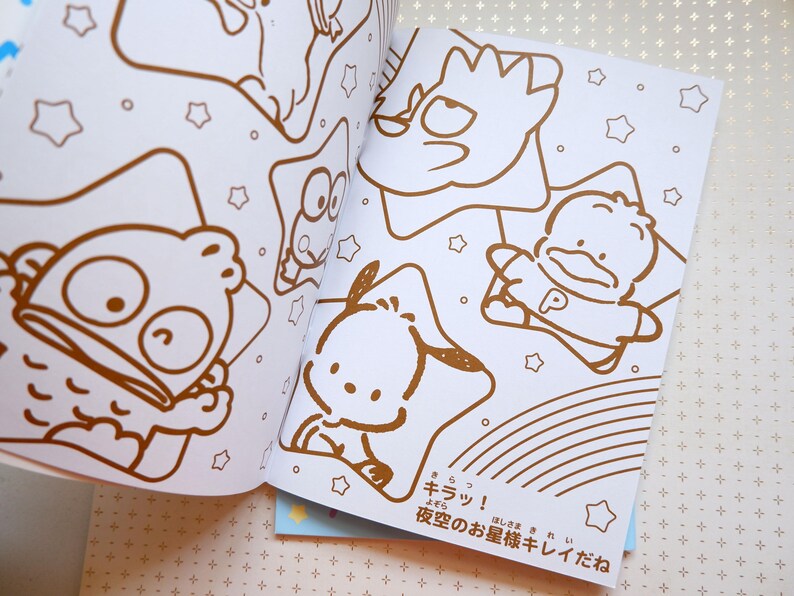 May include: A coloring book with a white background and brown outlines of various characters. The characters include a fish, a star, a duck, and a dog. The text on the page reads "キラッ! 夜空のお星様キレイだね".