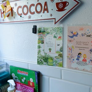 May include: Two framed illustrations on a white tiled wall. The illustration on the left is a colorful garden scene with the text "My Heavenly Garden". The illustration on the right is a pink and white scene with the text "Andersen's Fairy Tales" in a white banner.