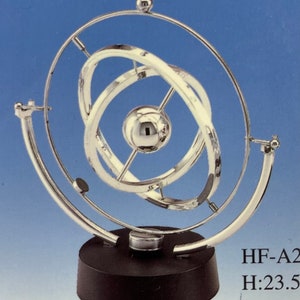May include: A silver-colored, three-dimensional, kinetic sculpture with multiple rotating rings and a central sphere. The sculpture is mounted on a black base. The height is 23.5 inches.