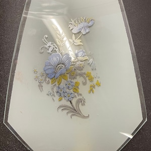 Peut inclure: Un panneau de verre transparent avec un motif floral. Le motif présente des fleurs et des feuilles bleues, jaunes et argentées. Le panneau mesure environ 15 cm de long.