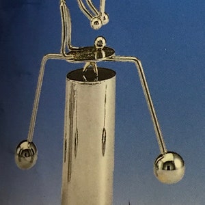 Puede incluir: Una escultura de metal plateado de un músico tocando el saxofón. La escultura tiene una base cilíndrica con una figura sentada encima, sosteniendo el instrumento. Dos brazos se extienden desde la base, cada uno terminando en una esfera plateada. El texto "HF-E20" está en la parte inferior.