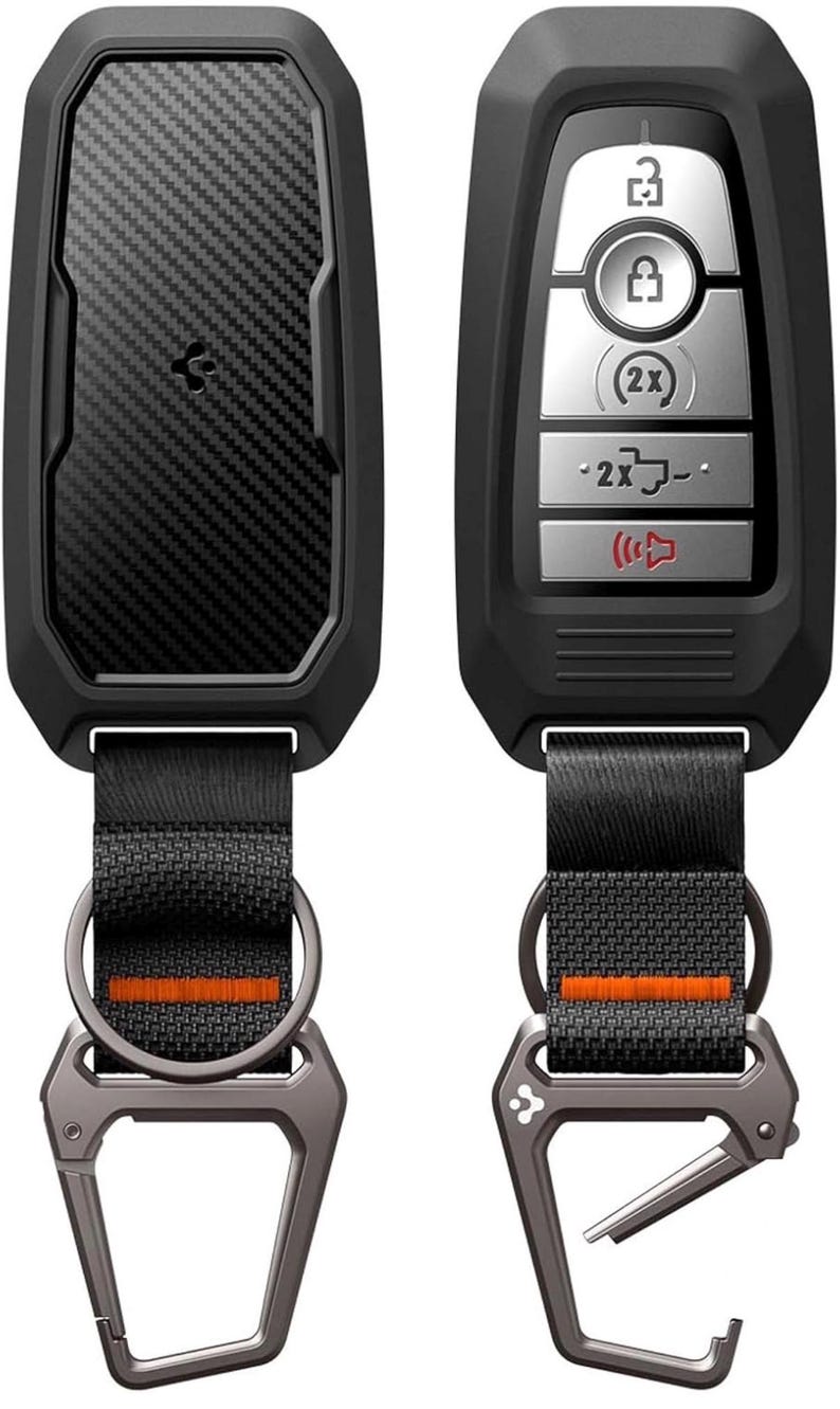 Puede incluir: Dos llaveros de coche negros con un dise&ntilde;o de fibra de carbono y un mosquet&oacute;n de metal. Uno tiene botones para bloquear y desbloquear, y el otro tiene un panel en blanco de fibra de carbono. Ambos tienen una correa negra con una raya naranja.
