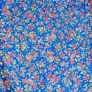 Könnte beinhalten: Ein leuchtend blauer Stoff mit einem sich wiederholenden Muster aus roten Paisley-Motiven und kleinen roten Rosen mit gelb-grünen Blättern. Das Design ist dicht gepackt und erzeugt eine reichhaltige und detaillierte visuelle Textur.