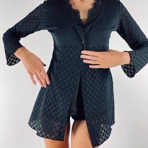 Puede incluir: Cárdigan negro con un patrón de diamantes en la parte inferior y las mangas. El cárdigan tiene un cuello de encaje y cierre de botón. Las mangas tienen un diseño acampanado en la muñeca. El cárdigan es de color oscuro.