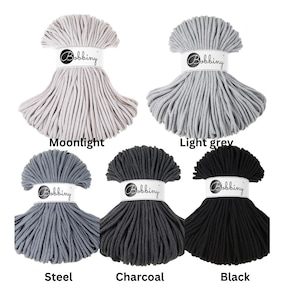 May include: Five hanks of Bobbiny cord arranged in a grid, featuring colors labeled Moonlight, Light grey, Steel, Charcoal, and Black. Each hank is secured with a white paper band displaying the Bobbiny logo in a black circular emblem.
