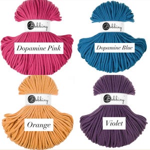 May include: Four skeins of Bobbiny cord arranged in a grid. The colors are Dopamine Pink, Dopamine Blue, Orange, and Violet. Each skein features a white paper label with the brand name Bobbiny and the specific color name printed in black text.