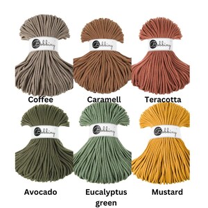 May include: Six skeins of Bobbiny cotton cord arranged in two rows. The colors are coffee, caramell, teracotta, avocado, eucalyptus green, and mustard. Each skein is secured with a white paper band featuring the Bobbiny logo in black text.